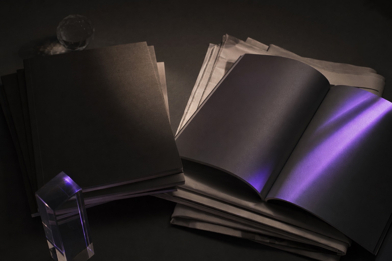 A still-life of unbranded magazines and newsprint on a dark surface lit by a violet beam